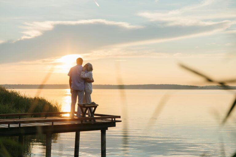 A happily retired couple embracing on a dock as they watch the sunset.